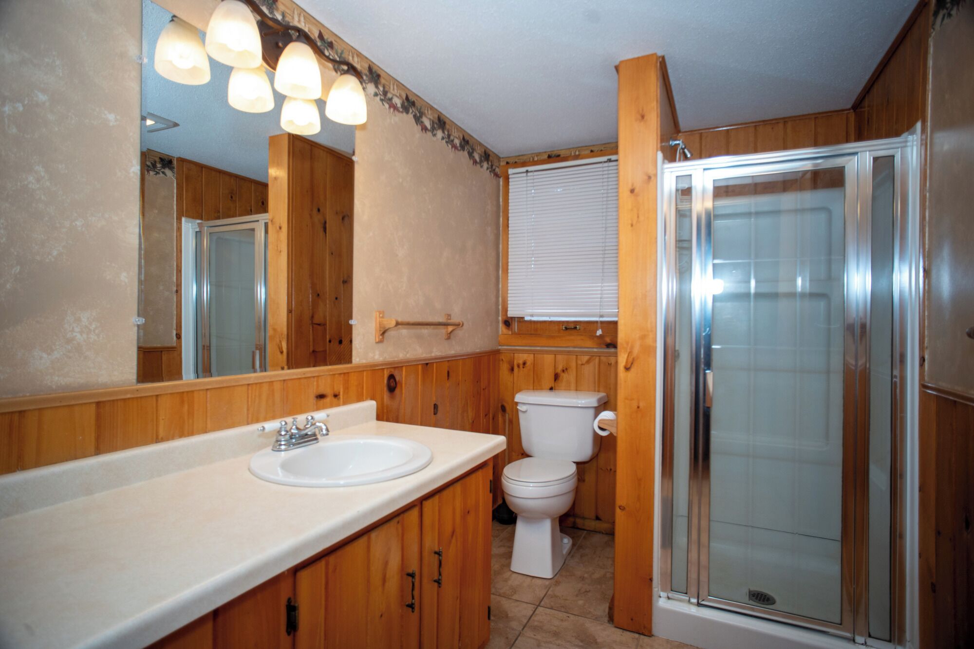 A bathroom with a wooden vanity, a sink, a toilet, and a glass-enclosed shower.