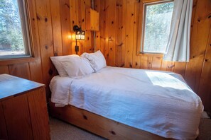 Ein Schlafzimmer einer Holzhütte mit einem Bett, Kissen, einem Nachttisch und einer Wandleuchte.