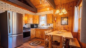 Eine rustikale Küche mit Holzschränken, einem Edelstahlkühlschrank, einer Mikrowelle und einem Holzessttisch mit Stühlen.