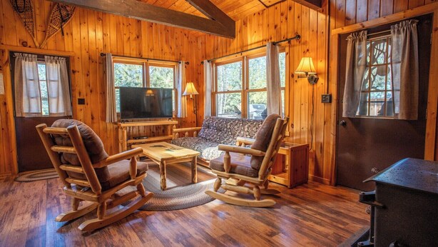 Ein Holzblockhaus-Interieur mit Kamin, Schaukelstühlen aus Holz, einer Couch und einem Fernseher.