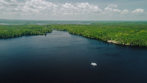 A river bordered by dense forests, a boat on the water, and a distant shoreline. - The Mallard Houseboat at Timber Bay (Babbitt)