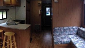 A compact RV interior with a kitchenette, a small bar area with stools, and a sofa. - The Mallard Houseboat at Timber Bay (Babbitt)
