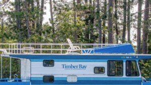 Un bateau appelé « Timber Bay », aux couleurs bleu et blanc, doté d’un pont couvert et d’une cabine avec des fenêtres.