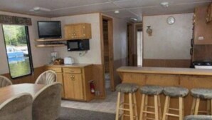 A compact living space with a kitchenette, a dining area with a table and chairs, a bar stool area, and a television mounted on the wall. - The Otter Houseboat at Timber Bay (Babbitt)