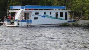A boat with a cabin, a deck, and a blue and green design on the side. - The Otter Houseboat at Timber Bay (Babbitt)