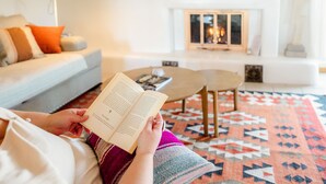 A person reading a book in a living room with a fireplace, a sofa, and a patterned rug.