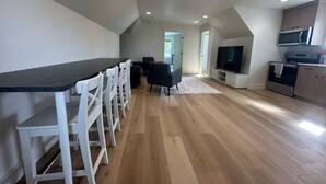 Et moderne køkken med mørkt bord, hvide stole, fjernsyn og indbyggede apparater.