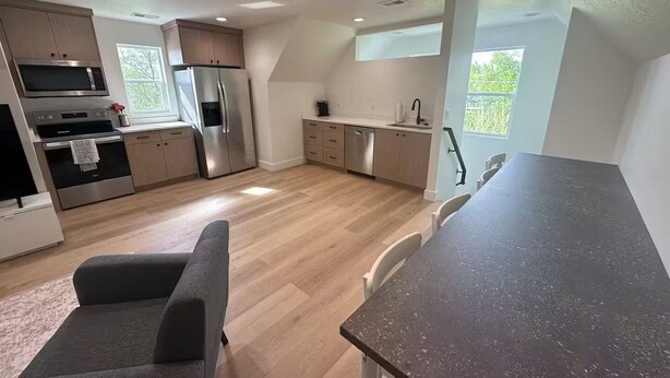 Et moderne køkken med stålemmer, et spiseområde med mørk bordplade og udsigt til grønne omgivelser.