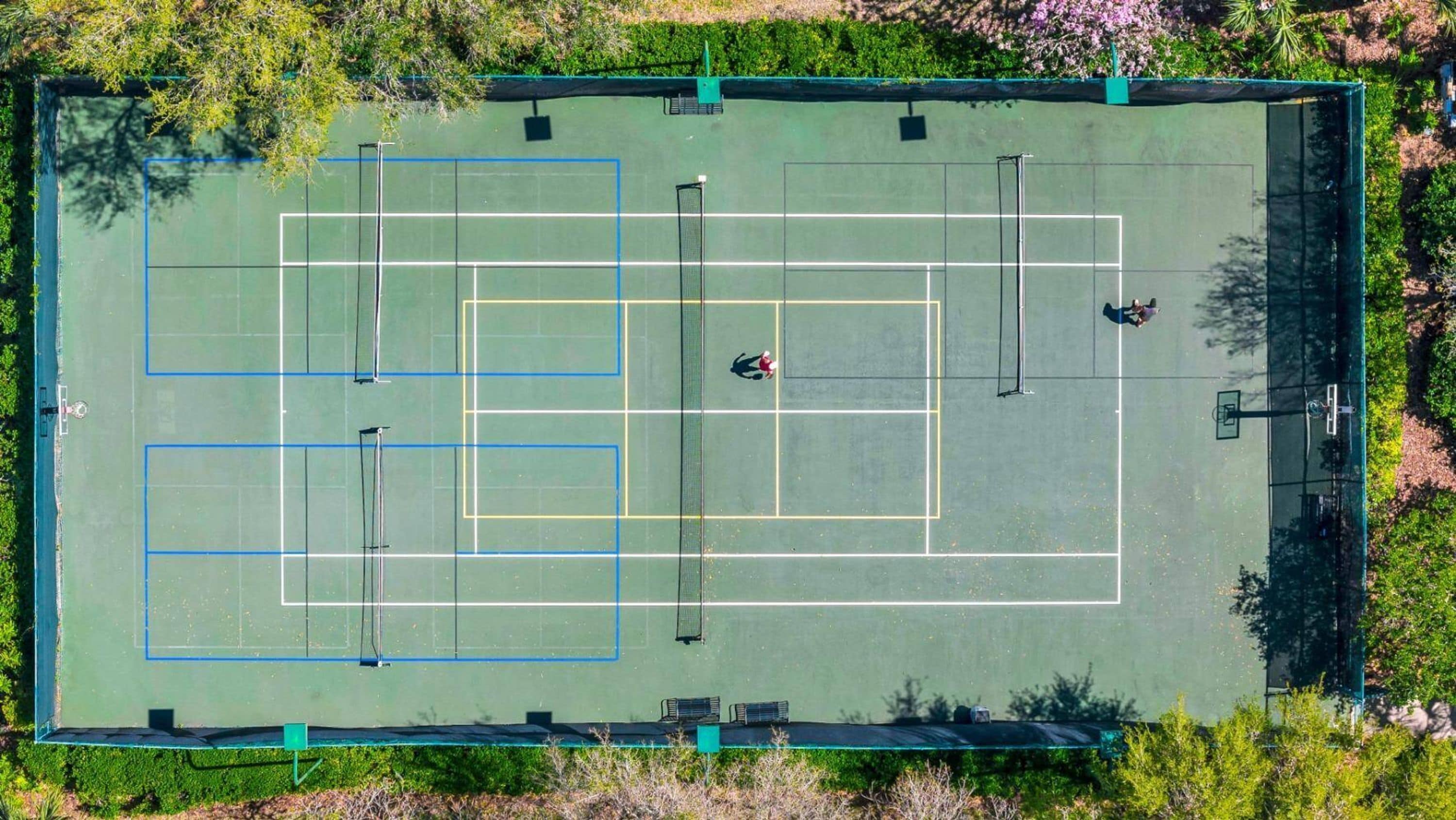 Eine Vogelperspektive auf einen Tennisplatz mit mehreren Spielfeldern, umgeben von Grünflächen.