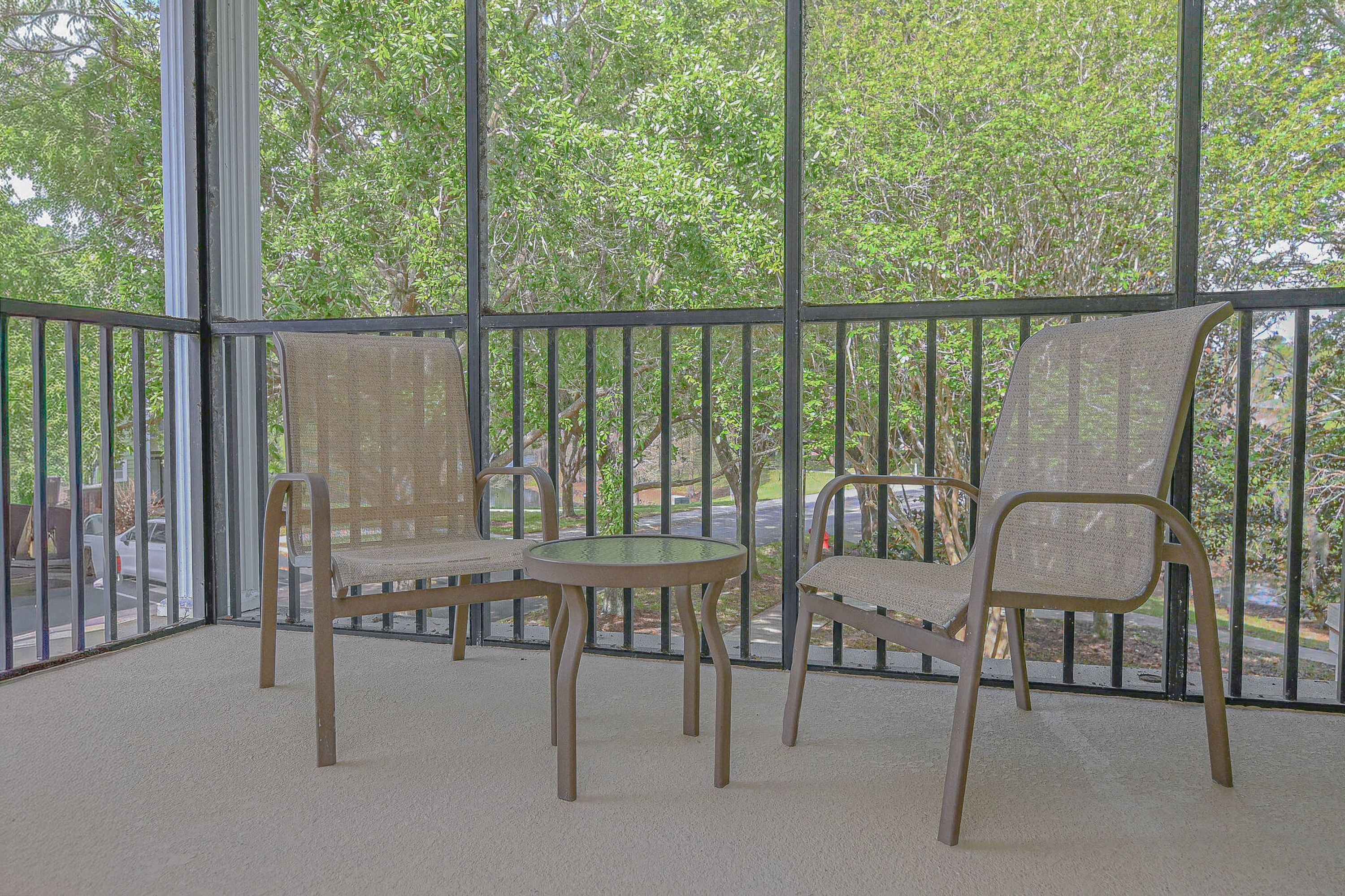 A balcony with two chairs and a table, surrounded by metal railings, overlooking a street and trees.