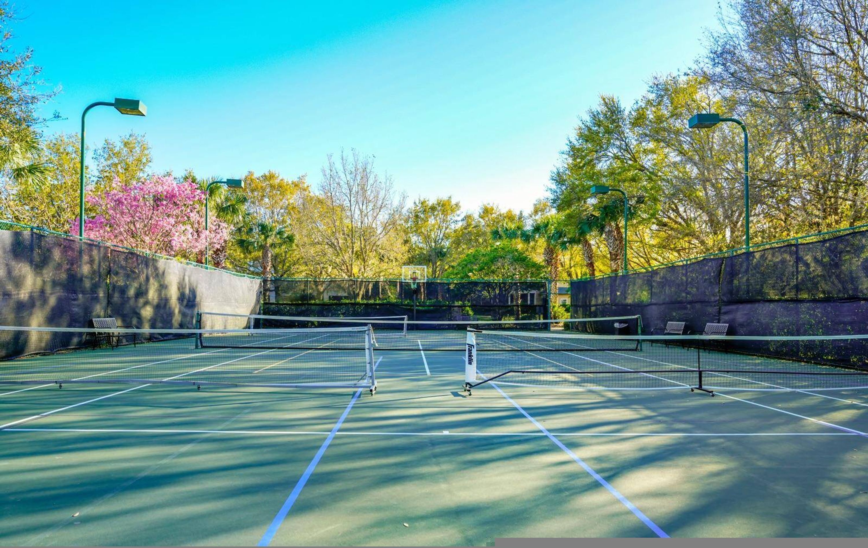 An outdoor tennis court with a net, surrounded by trees and a stone wall.