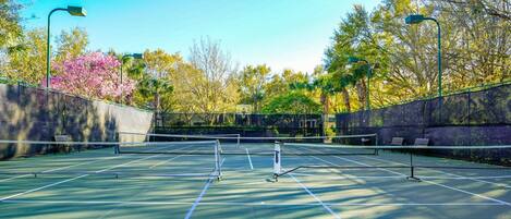 An outdoor tennis court with a net, surrounded by trees and a stone wall.