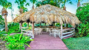 A thatched-roof outdoor pavilion with tables and chairs, surrounded by lush greenery and palm trees. - Go 13 - Bahama BAY in Davenport (Davenport)