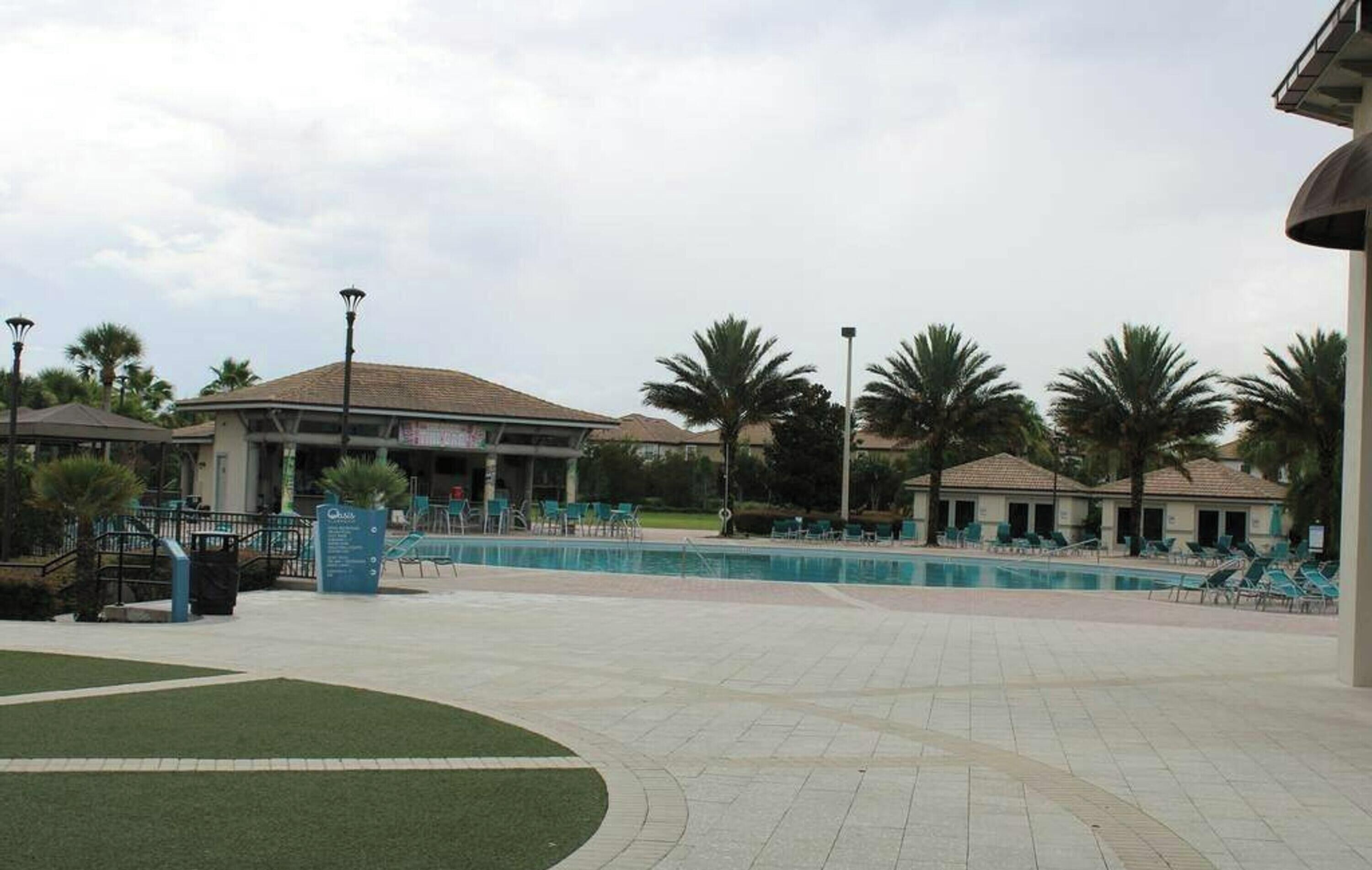 A pool area with lounge chairs, palm trees, and a building with a tiled roof.