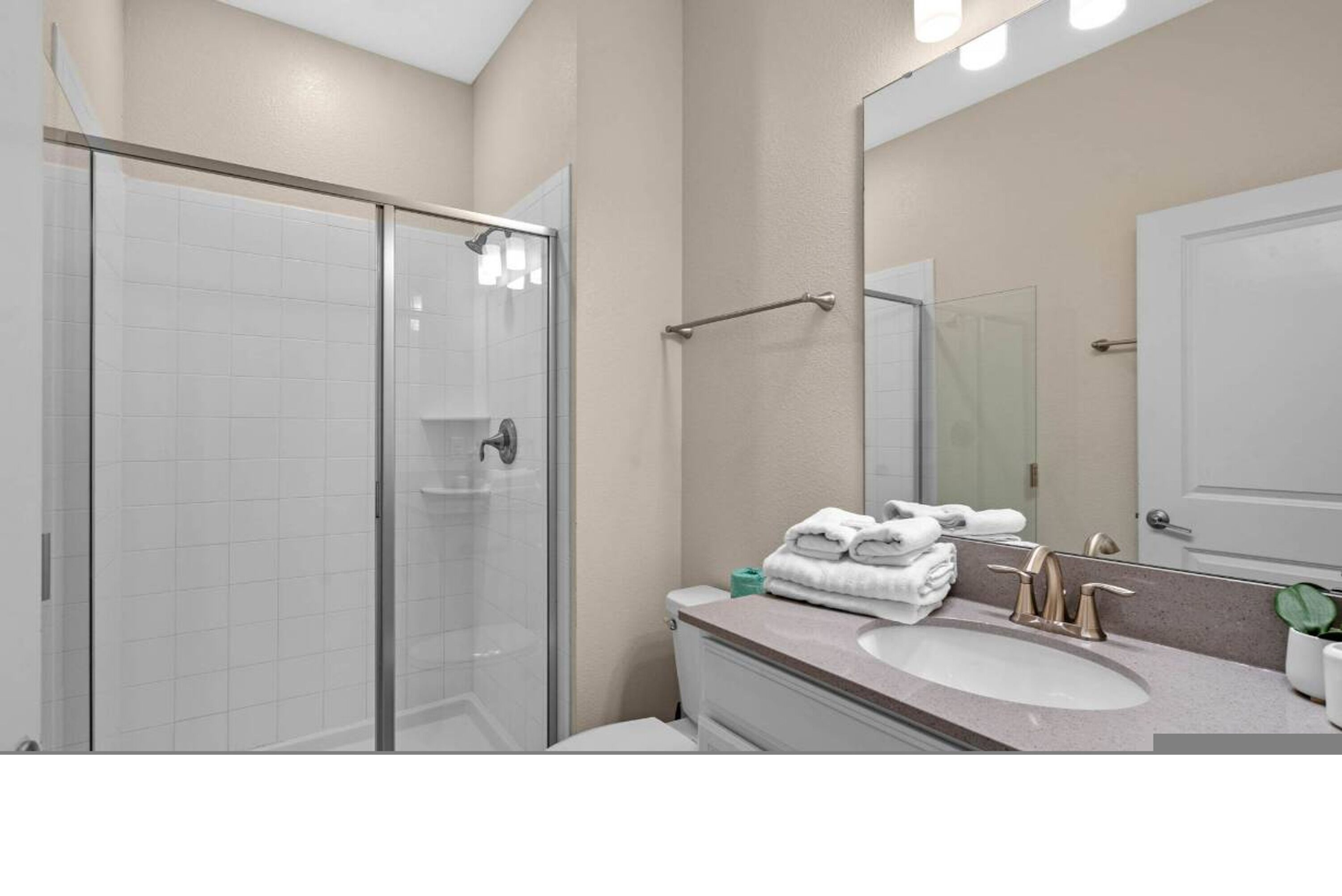 A bathroom with a glass shower enclosure, a sink with a vanity, and a large mirror.