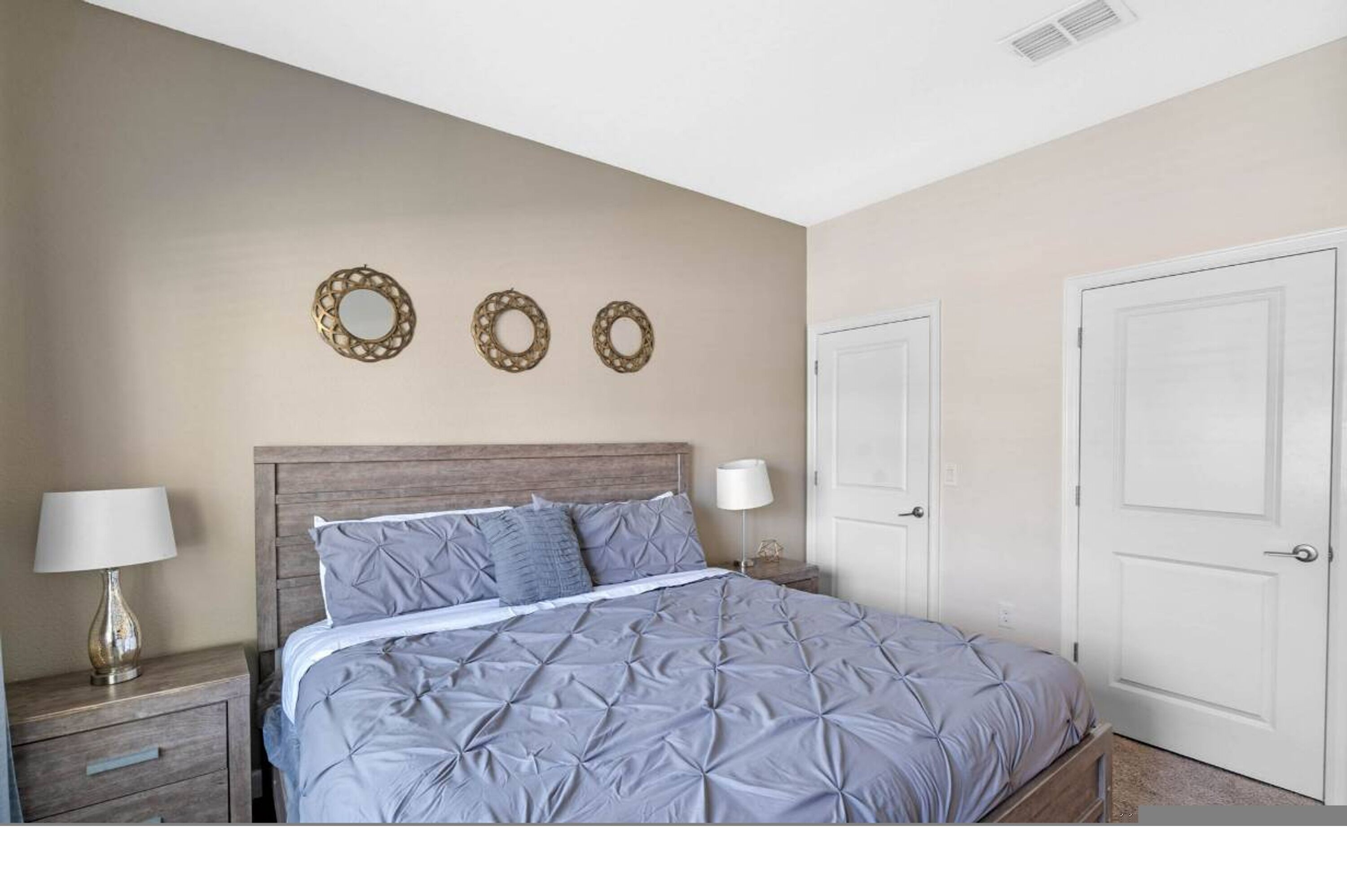A bedroom with a bed, two nightstands, a wooden headboard, and two doors.