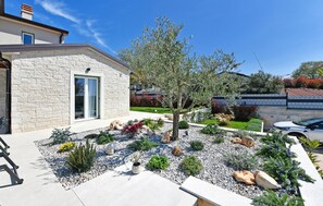 A modern house with a stone facade, a well-maintained garden with various plants and a tree, and a parked car in the driveway. - Awesome home in Porec (Porec)