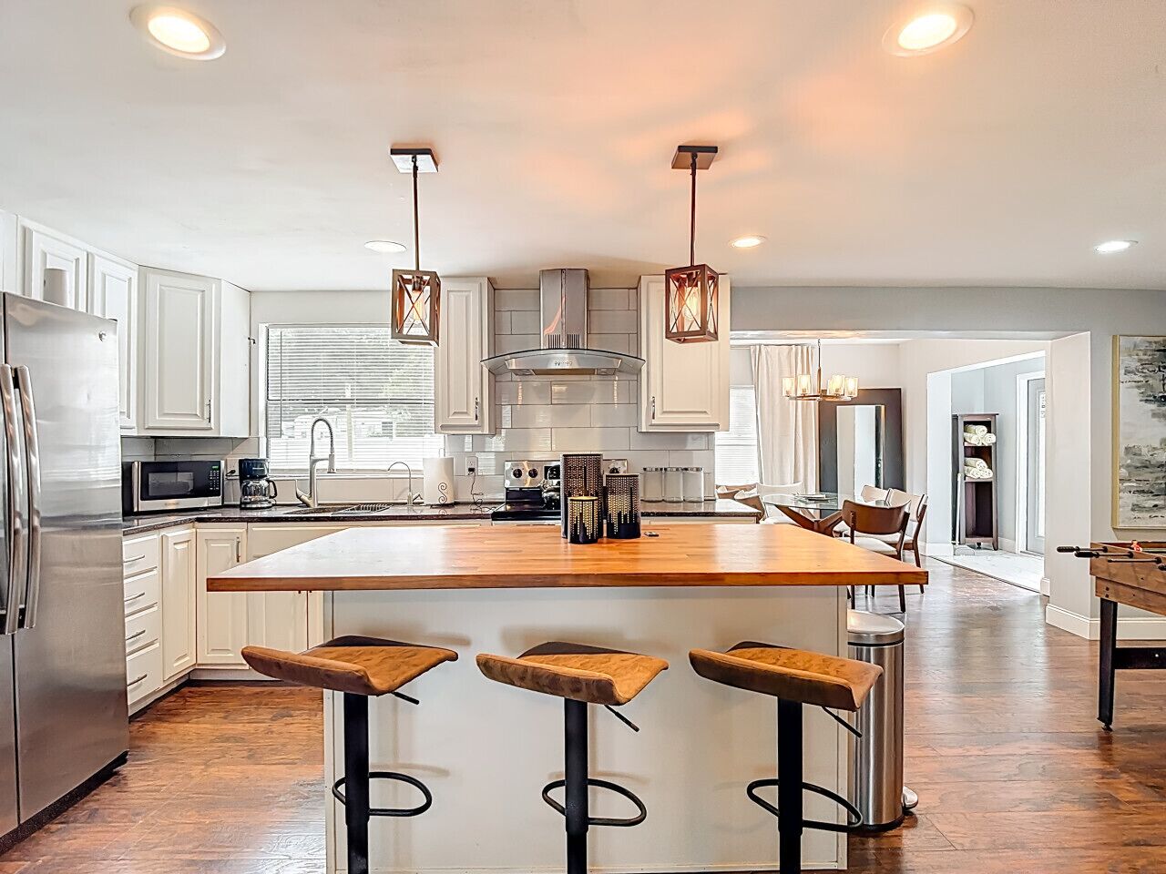 A modern kitchen with white cabinets, a central island with stools, and pendant lighting.
