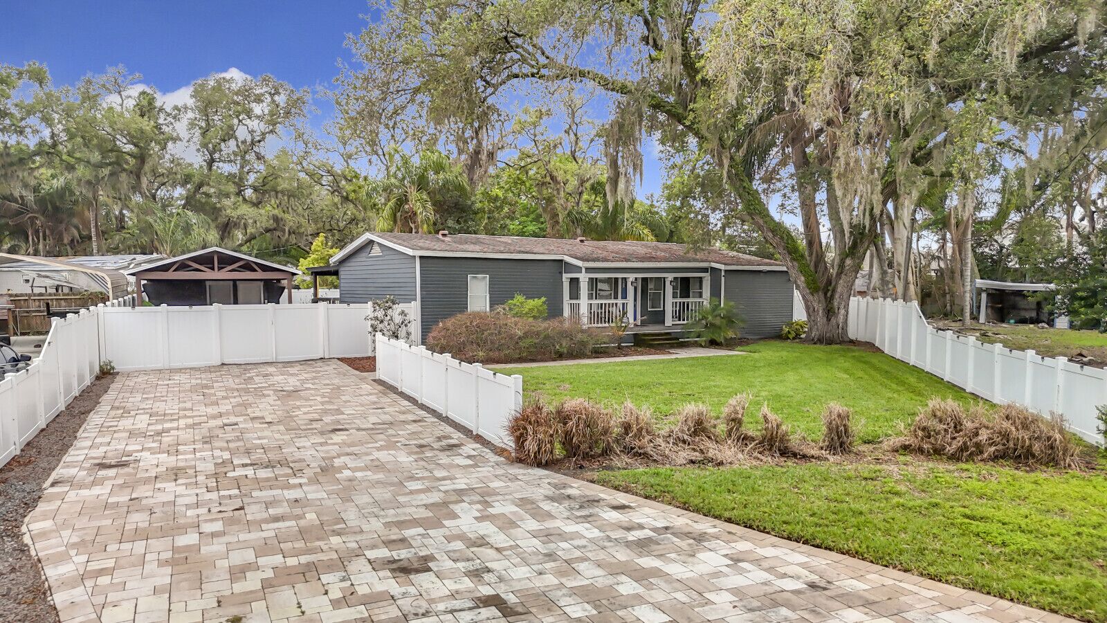A residential property with a paved driveway, a fenced yard, and a house with a porch.