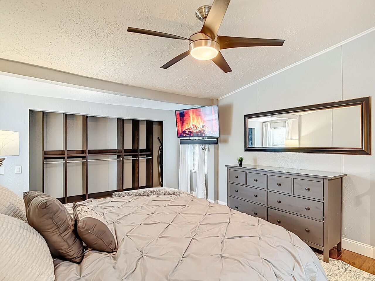 A bedroom with a bed, a dresser, a ceiling fan, a TV, and a window with blinds.