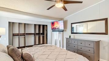 A bedroom with a bed, a dresser, a ceiling fan, a TV, and a window with blinds.
