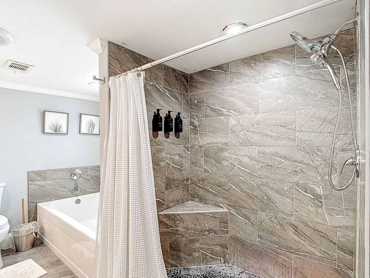 Een moderne badkamer met een badkuip, douche en marmeren wanden.
