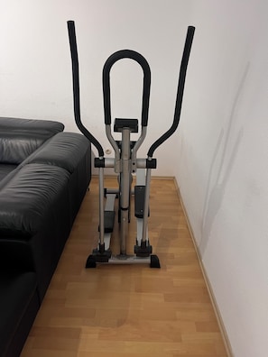 Ein stationäres Fahrrad in einem Zimmer mit Holzboden und einem schwarzen Ledersofa.