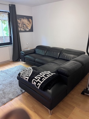 Um sofá de couro preto com um cobertor estampado, uma pequena mesa lateral com abajur e um quadro na parede.