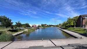 Kanava, jonka varrella on jalankulkijoiden käytävä, ja taustalla näkyy puita ja rakennuksia.