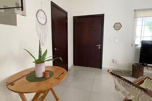 Ein Zimmer mit einem Holztisch, einer Topfpflanze, einem Traumfänger und einem Fernseher.