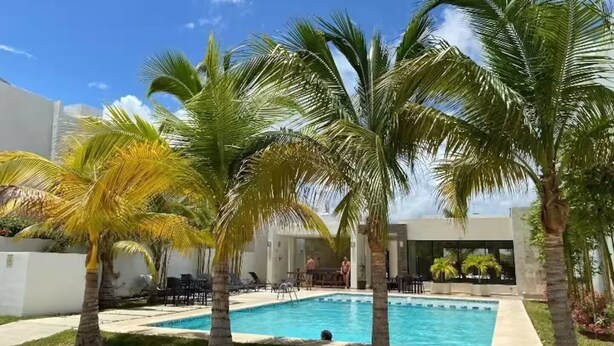 A pool area with palm trees, lounge chairs, and a building in the background. - Cozy House in Selvanova 3B (Playa del Carmen)