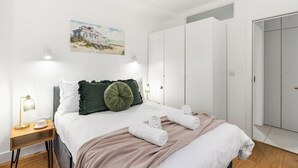 A neatly arranged bedroom with a bed, bedside tables, a painting, and a wardrobe. - Stylish Seaside Apartment | Minutes from Beach (Eastbourne)