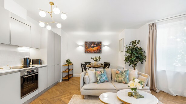 A modern kitchen with white cabinets, a built-in oven, and a dining area with a sofa and coffee table. - Stylish Seaside Apartment | Minutes from Beach (Eastbourne)
