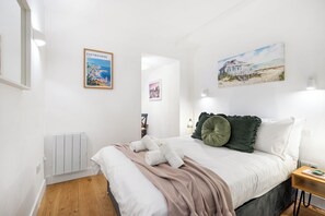 Une chambre à coucher avec un lit, un radiateur, un plancher en bois et des œuvres d’art murales.