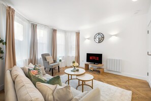 Un salon moderne avec un canapé, des fauteuils, une table basse, un téléviseur et une horloge au mur.