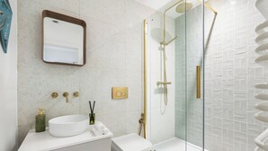 A modern bathroom with a white sink, a toilet, a glass-enclosed shower, and a mirror. - Stylish Seaside Apartment | Minutes from Beach (Eastbourne)