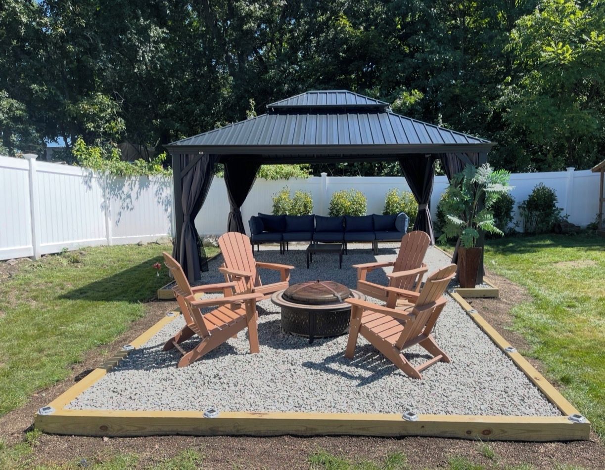 A gazebo with a fire pit and Adirondack chairs in a backyard.
