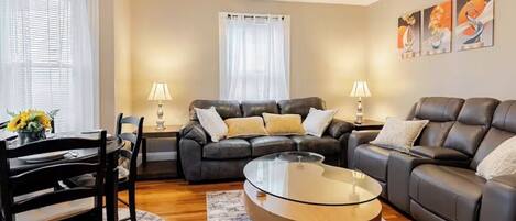 A living room with a glass coffee table, two sofas, a dining table with chairs, and lamps.