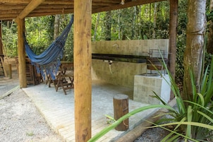 Uma pérgola de madeira com uma rede, uma pia de pedra e um banco.