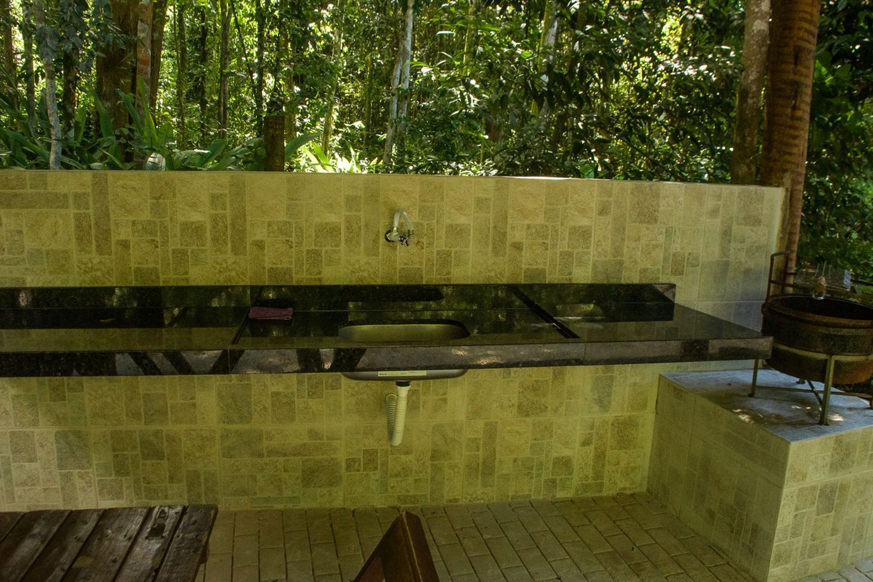 Una cocina al aire libre con pileta integrada, una olla sobre un soporte y una mesa de madera.