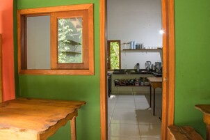 Cozinha com parede verde, mesa de madeira e janela com vista para vegetação.