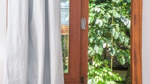 Ein Fenster mit Holzrahmen und Metallgriff, mit Blick auf einen Garten mit grünem Laubwerk.