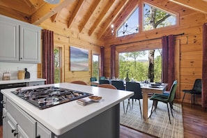 A wooden cabin interior with a kitchen, dining area, and large windows. - Best of Blue Ridge | Hot Tub |  Games | Pickleball (Blue Ridge)