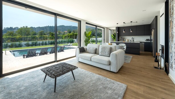 Ein modernes Wohnzimmer mit Sofa, Couchtisch und Blick auf einen Swimmingpool und Grünflächen.