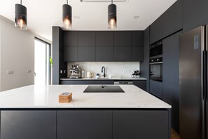 A modern kitchen with dark cabinetry, a marble countertop, and stainless steel appliances. - 202 - Casinha da Ribeira (Vila Verde)