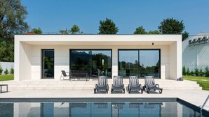 Ein modernes Haus mit Pool, Sitzgelegenheiten im Freien und großen Fenstern.