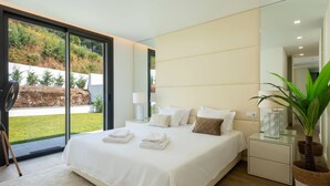 Ein modernes Schlafzimmer mit einem großen Bett, Nachttischen, einem Spiegel und Blick auf einen Garten.