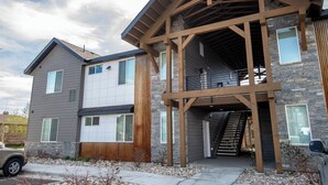 A modern two-story house with a stone facade, a wooden deck, and a covered staircase. - Two-bedroom Flat at Teton Peaks (Driggs)