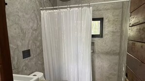 Bany amb cortina de dutxa, vàter i finestra petita.