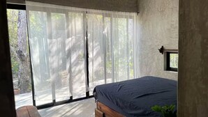 Een slaapkamer met een bed, een bankje en uitzicht op de omgeving door grote ramen.
